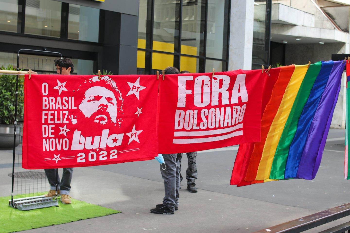 People hold political banners and a rainbow flag outdoors.